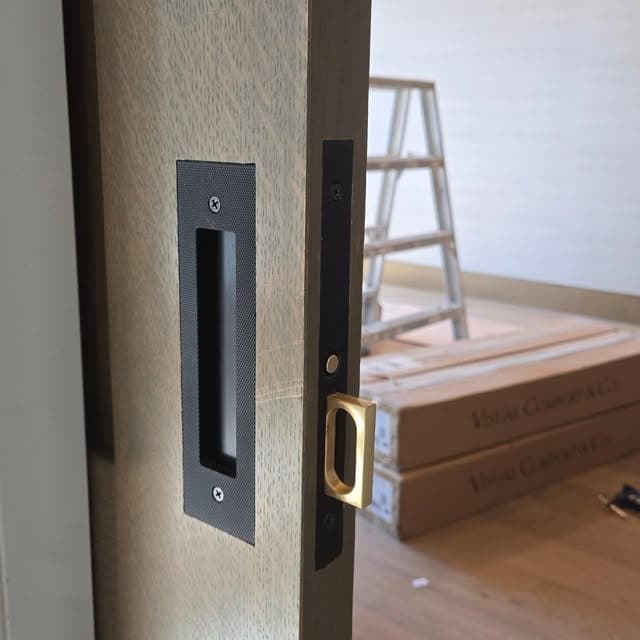 Close-up of brass and black recessed pocket door hardware being installed