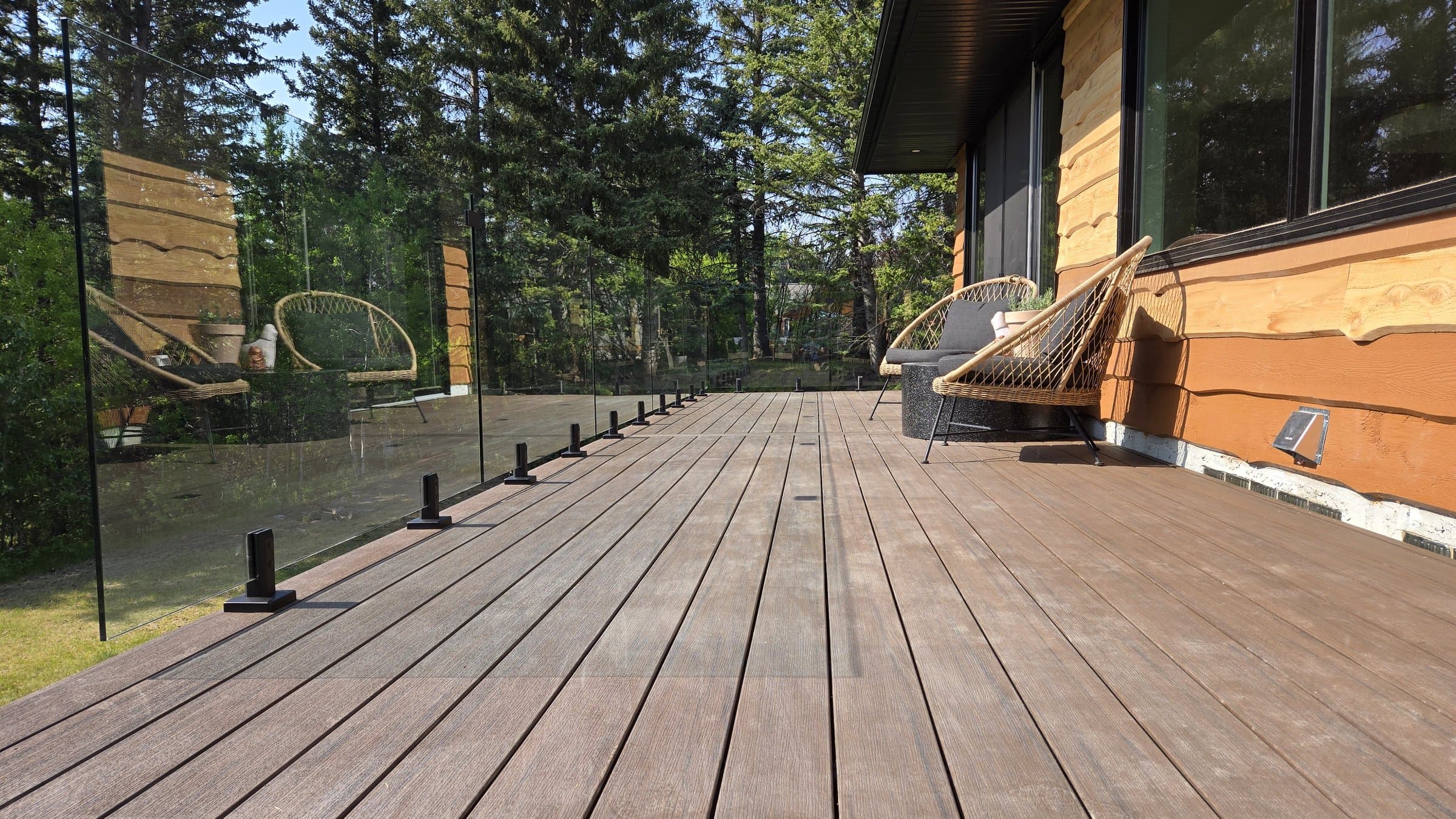 Finished composite deck with frameless glass railing beside a log-style home
