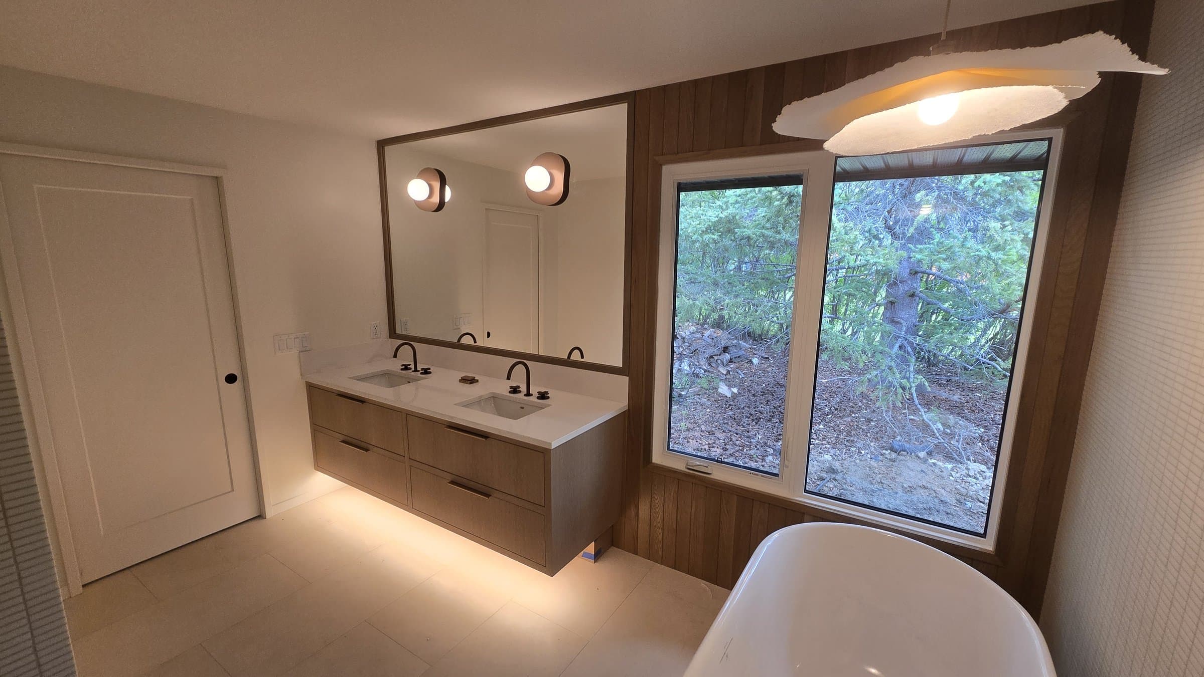 Floating double vanity, backlit toe-kick, wood accent wall, and freestanding soaker tub