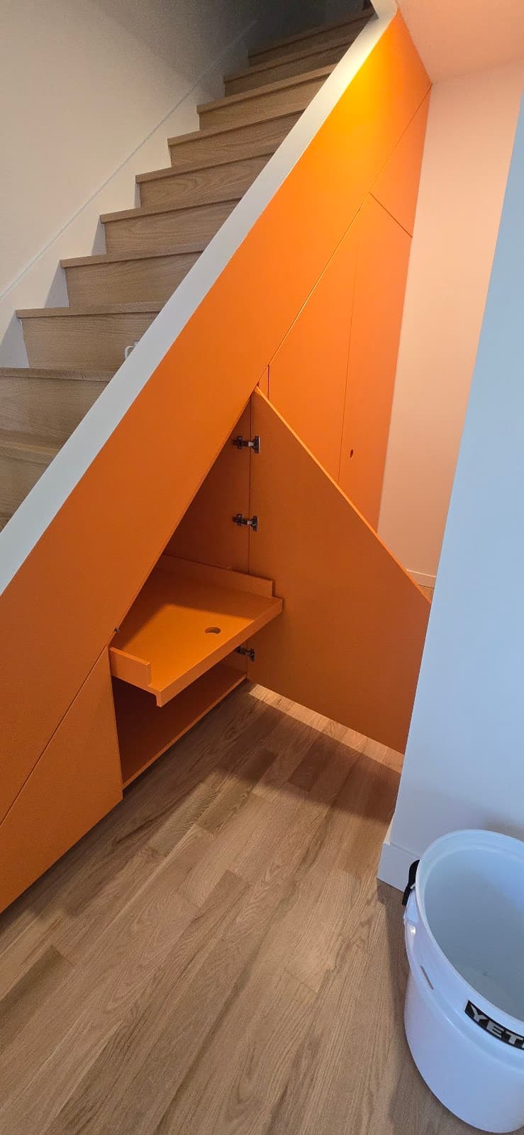Custom-built orange under-stair storage cabinetry with angled doors matching the stair line